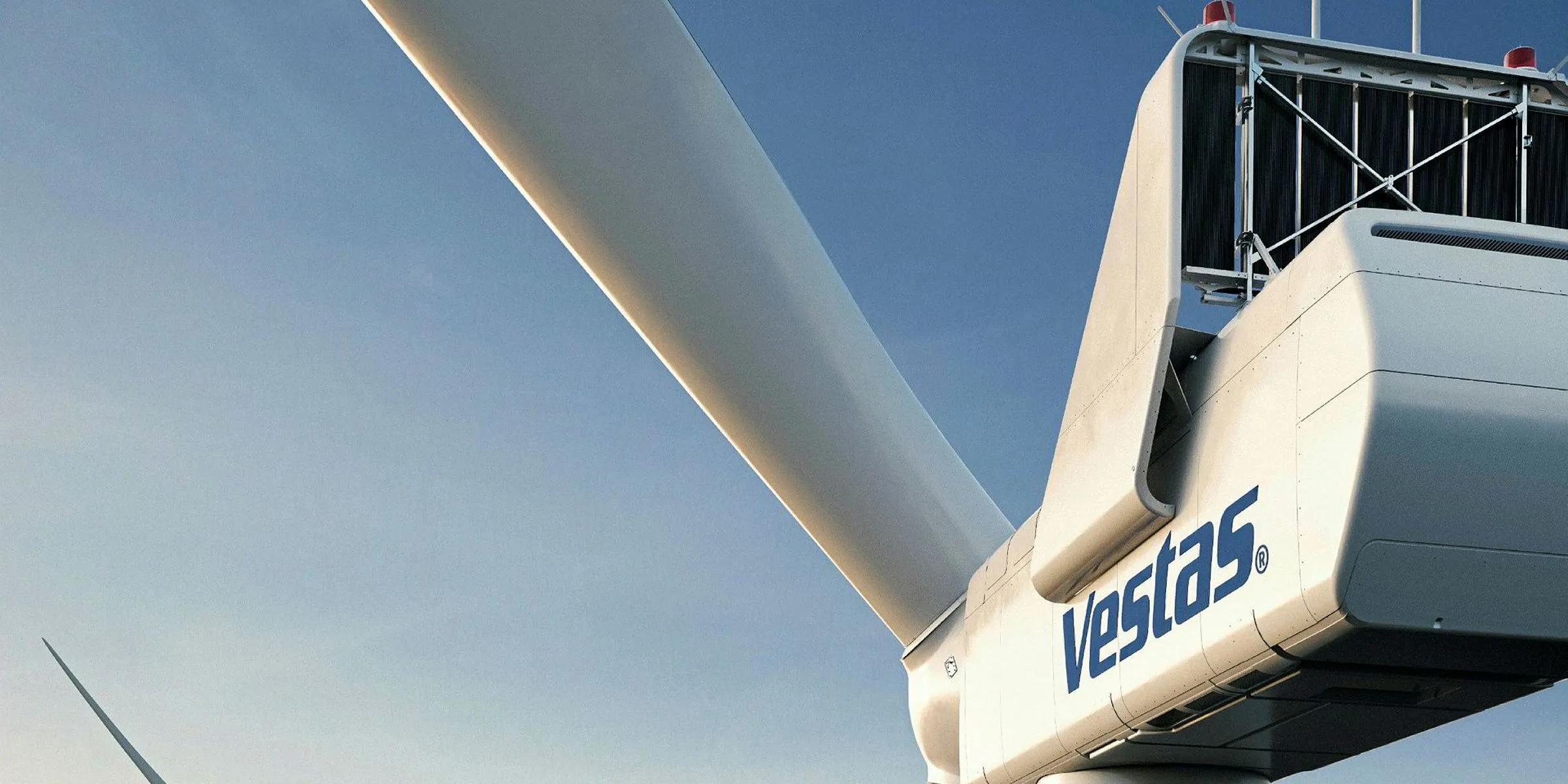 Close-up of a white Vestas wind turbine nacelle with a large blade attached against a clear blue sky