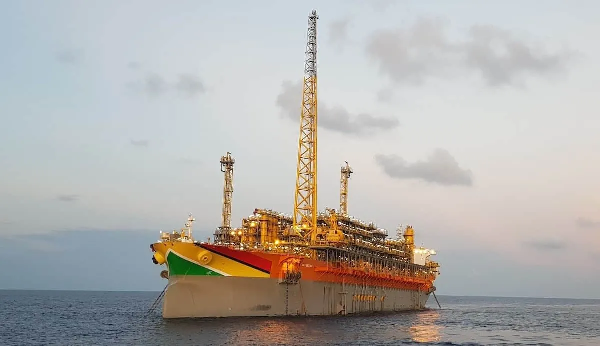 Colorful offshore oil platform vessel with tall cranes anchored in calm sea at sunset