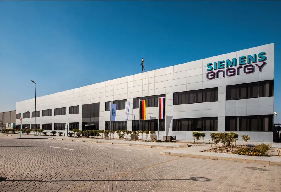 Siemens Energy office building with blue sky, glass windows, and flags in front of a paved parking area.
