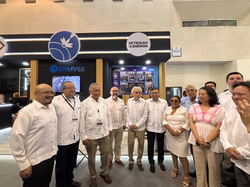 WhatsApp Image 2026-09-08 at 11655 PM - Petróleo y Energía Group of people in white shirts posing for a photo at an expo booth with 'SPIMVER' and 'Petróleo & Energia' signage in the background.