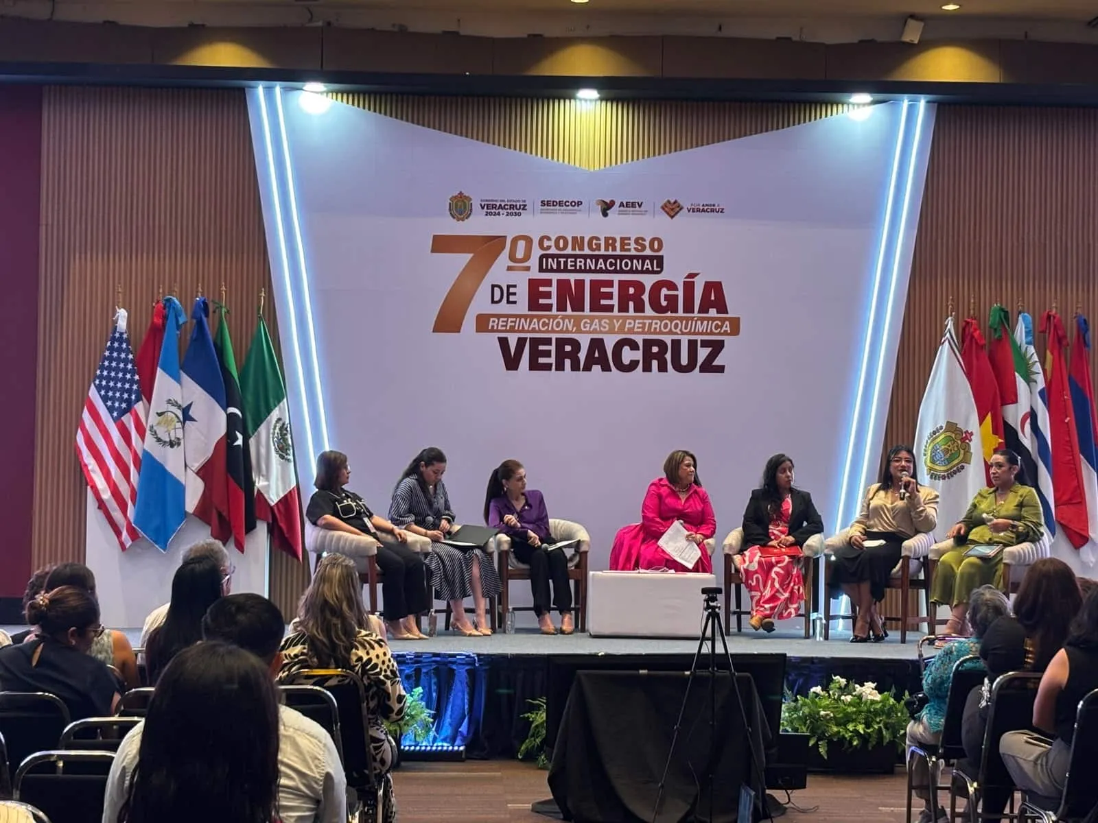 Panel of speakers seated on a stage at an international energy congress in Veracruz, with multiple flags behind and a large banner reading '7o Congreso Internacional de Energía Veracru z'.