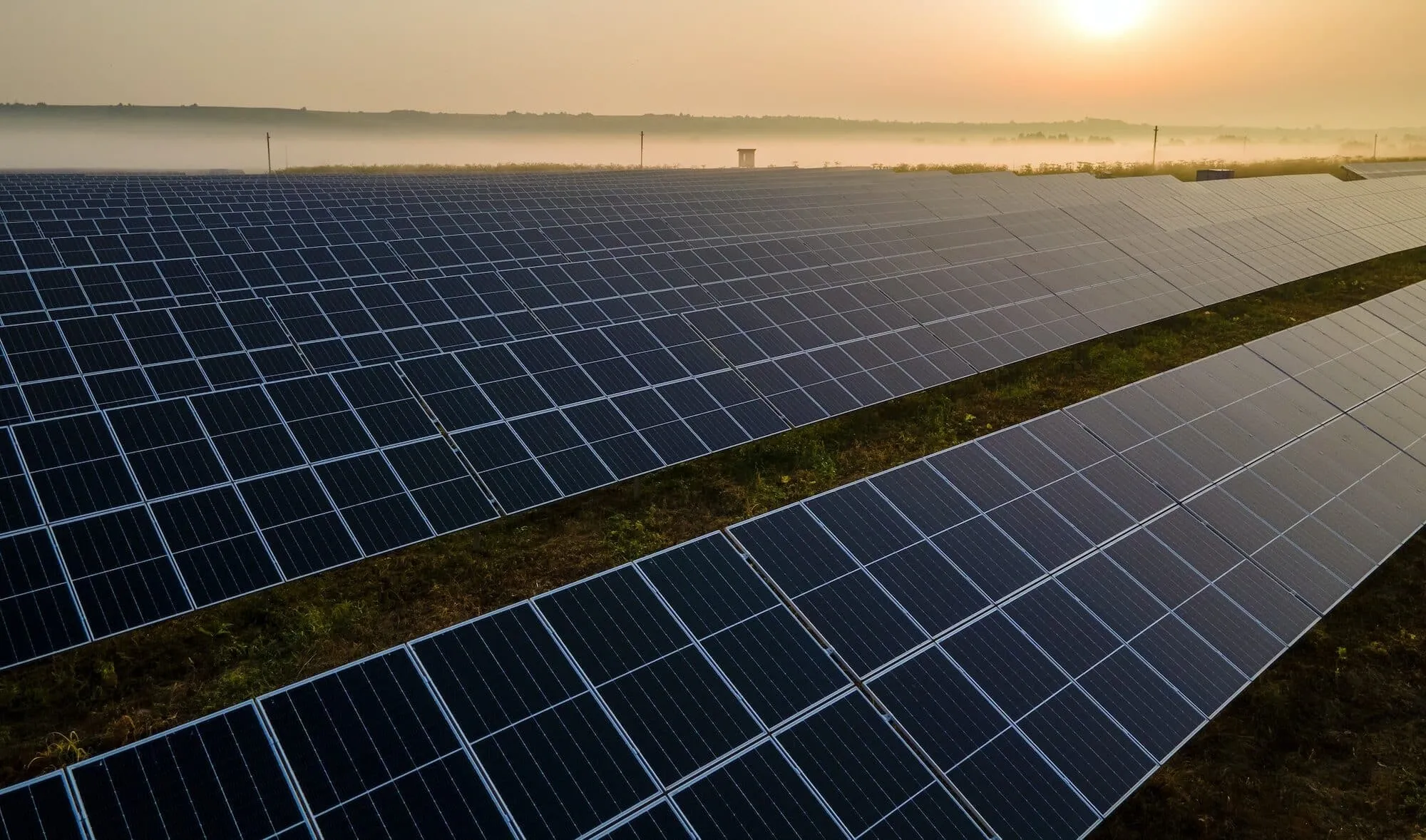 Wide field of solar panels at sunrise, stretching to the hazy horizon, illustrating a solar farm and clean energy.