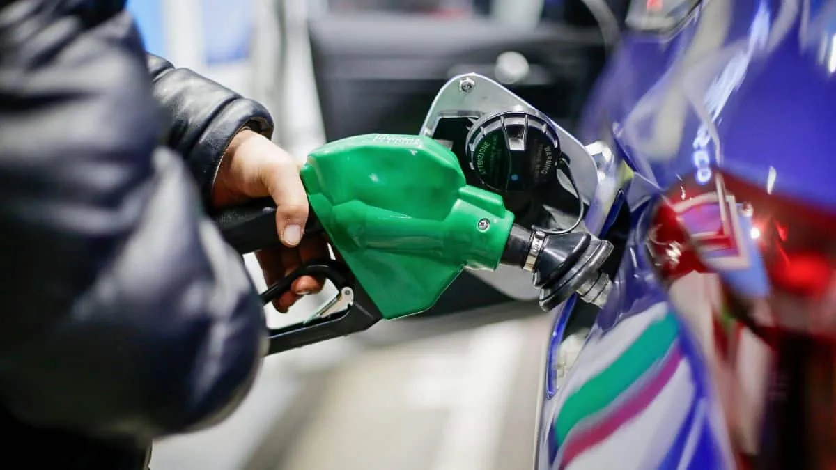 Person pumping gas into a blue car using a green fuel nozzle at a station.