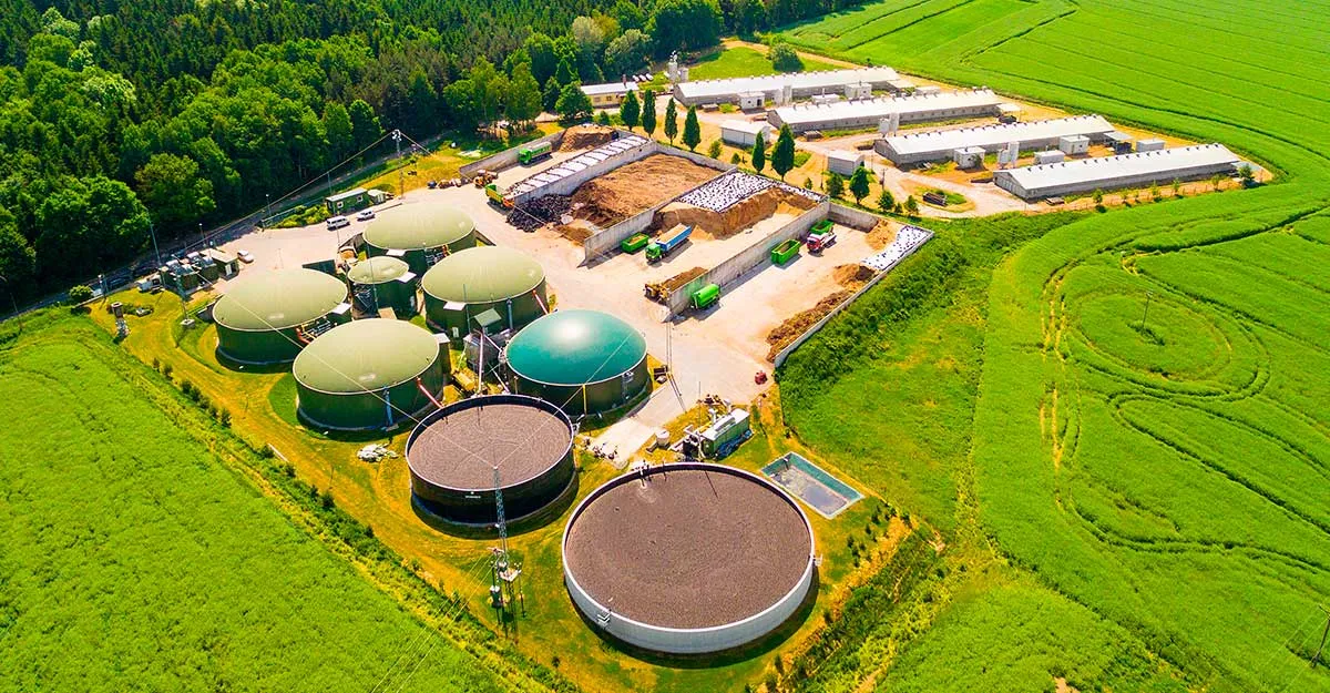 Aerial view of a rural industrial facility with several large circular storage tanks and green fields surrounding it.