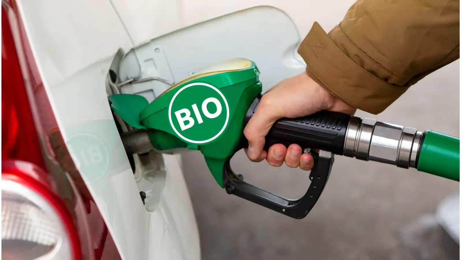Hand gripping a green biofuel pump nozzle inserted into a car's fuel filler, with a BIO label on the nozzle