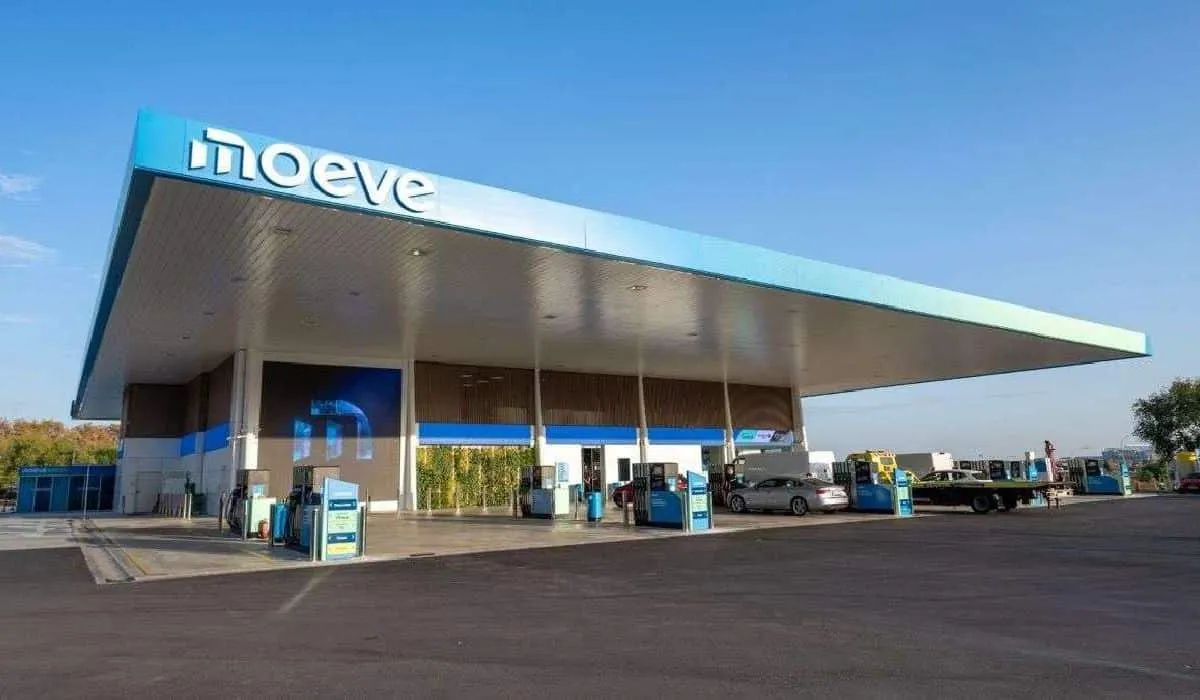 Gas station with a large slanted blue canopy and multiple fueling islands, cars refueling under a sunny sky