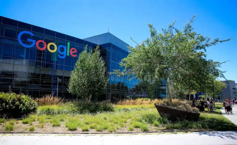 Google logo on a glass-front building with landscaped foreground and blue sky above.