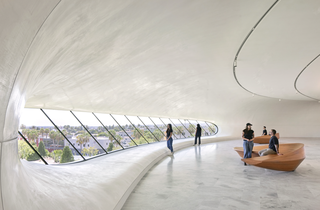 museo lucas 2026-09-23 a las 94906 am - Petróleo y Energía Open, curved white interior with large diagonal windows and several people standing or sitting on curved wooden benches.