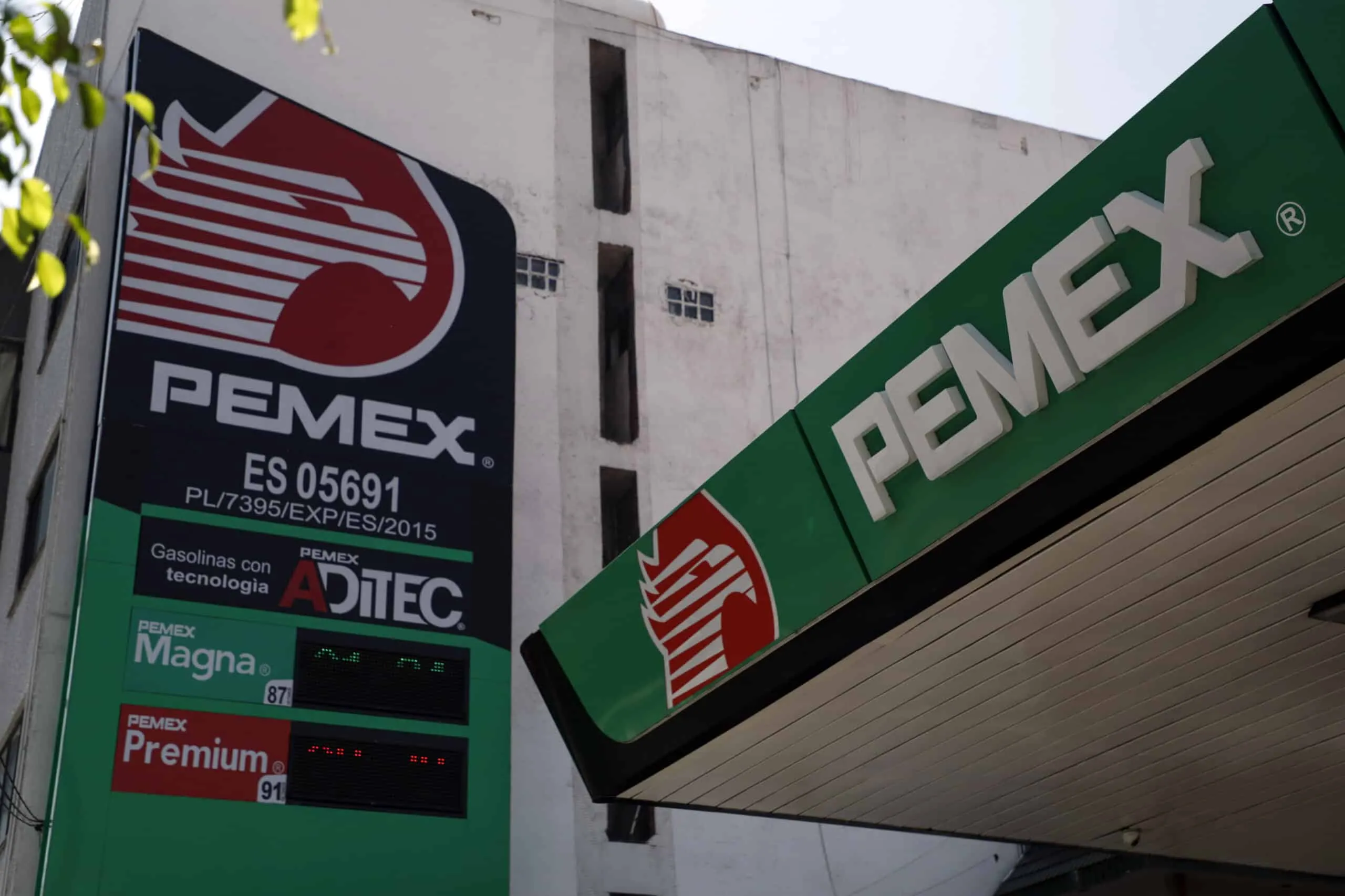 Gas station storefront with PEMEX branding and large green canopy displaying fuel ads and logos — diagonally viewed corner.