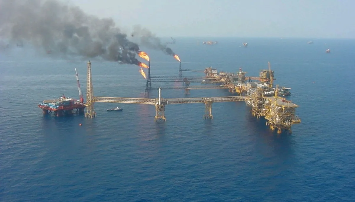 Offshore oil platform with two flaming vent flames and black smoke rising over the sea.
