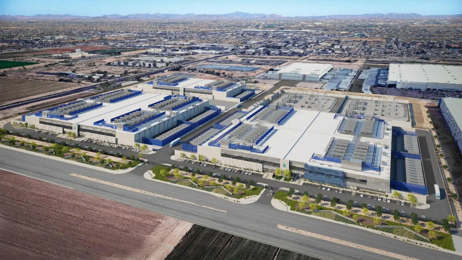 Large industrial complex with white and blue warehouses, solar panels on the roofs, set in a desert landscape with wide roads.