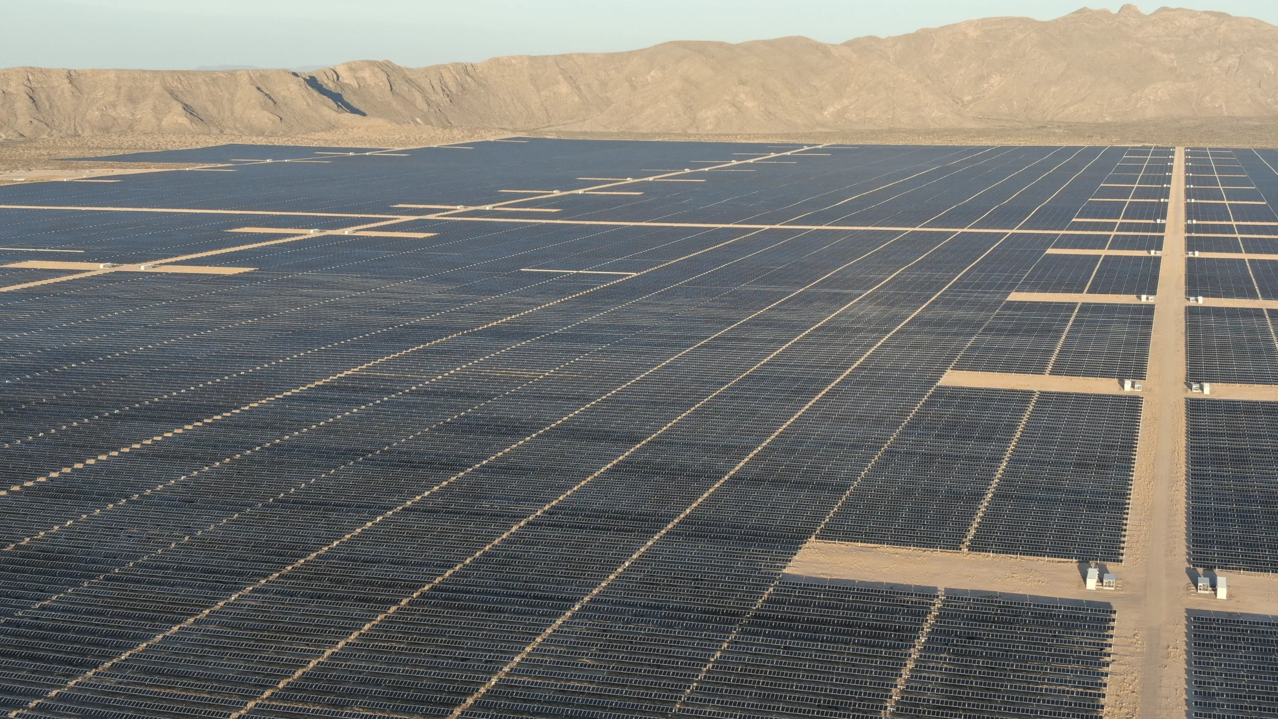 Extensive solar panel fields spanning a desert landscape with distant rocky hills in the background