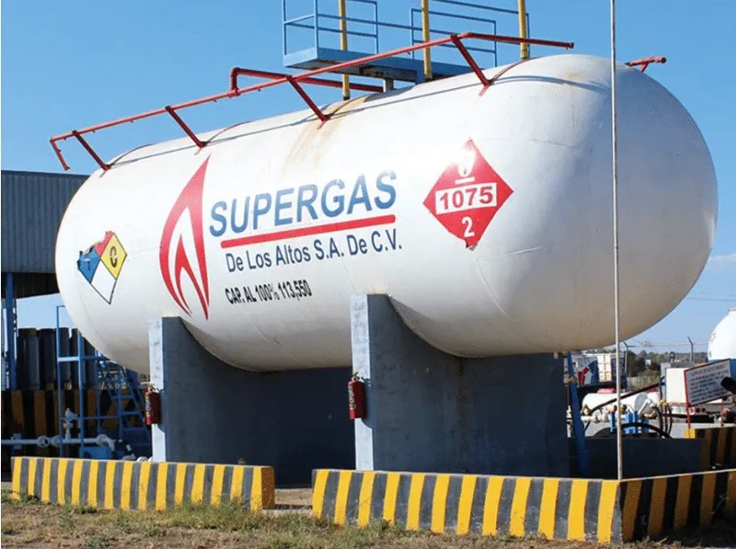 Large white propane storage tank labeled SUPERGAS, raised on concrete supports at an industrial facility, with hazard diamond markings