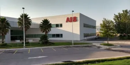 Exterior view of an ABB office building with palm trees, a manicured lawn, and a parking lot in front under a clear sky