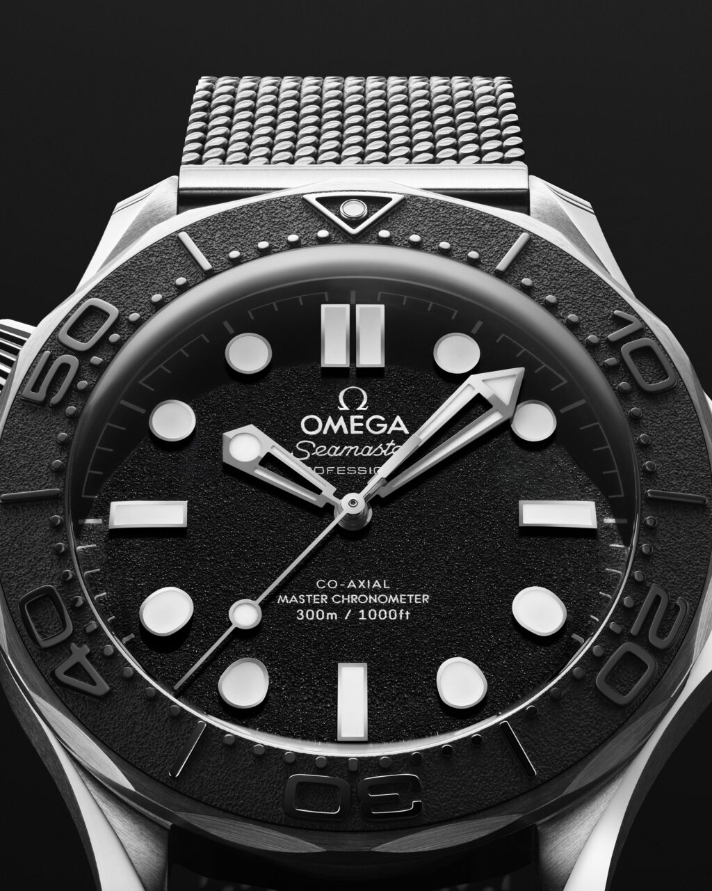 21030422001023_BondSpectre_ADV_SE_CU_Cadran_4_5_RVB - Petróleo y Energía Close-up of an Omega Seamaster watch face with textured black dial, bold white markers, and metallic bezel detail.