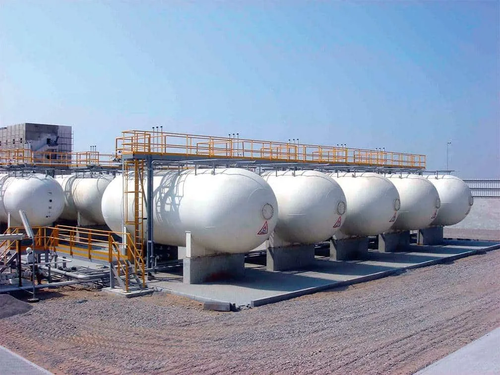 Row of large white cylindrical storage tanks on a rooftop facility, with yellow safety railings and piping overhead and a clear blue sky above.