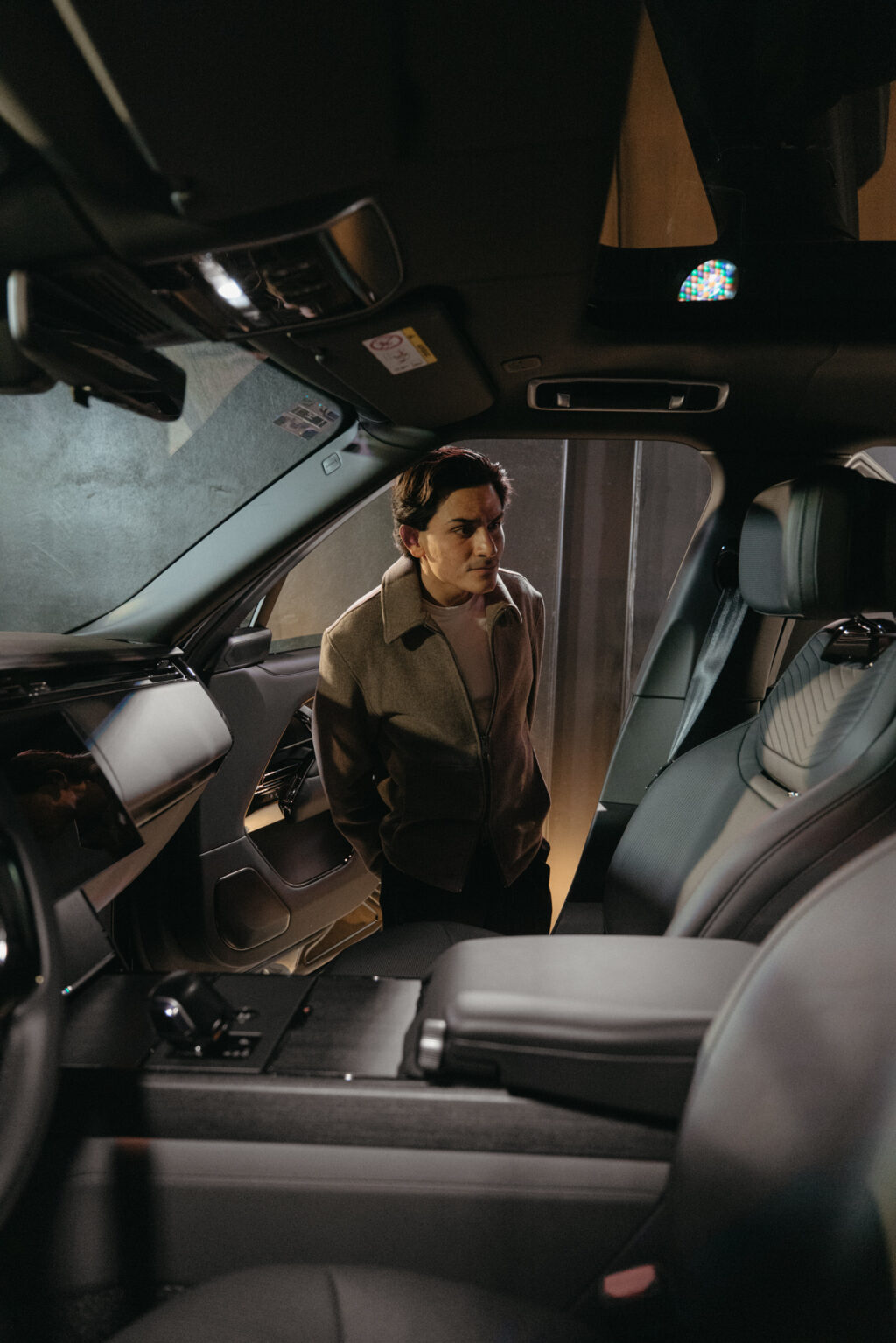 Range Rover - Petróleo y Energía Man wearing a brown jacket stands beside an open car door, leaning into the front cabin and looking inside the vehicle.