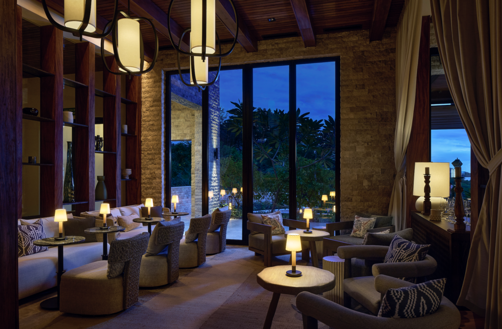5 EXCUSAS GOURMET 2026-10-15 a las 32214 pm - Petróleo y Energía Upscale lounge with wicker chairs, round tables, and warm pendant lighting, near large windows looking out at a blue twilight scene.