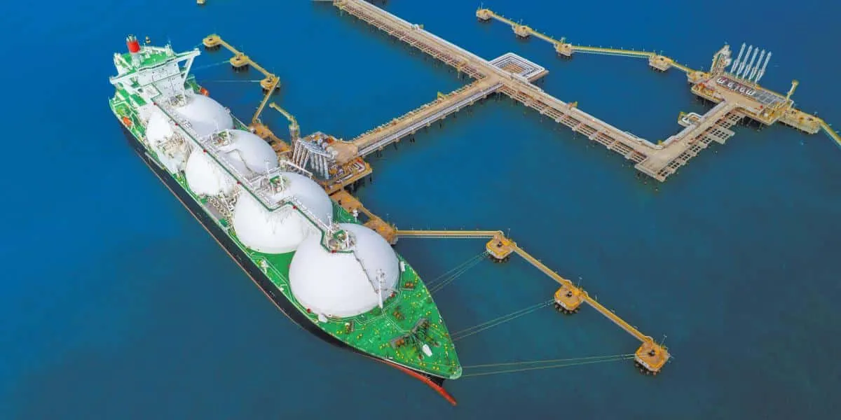 LNG tanker docked at an offshore loading terminal with pipelines connecting to the platform in calm blue water and clear skies.