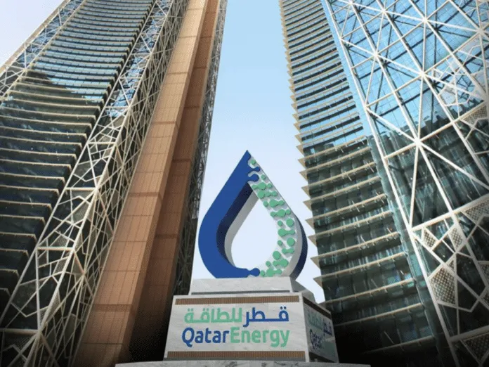 QatarEnergy logo sculpture between two tall modern buildings, with Arabic and English text at the base.