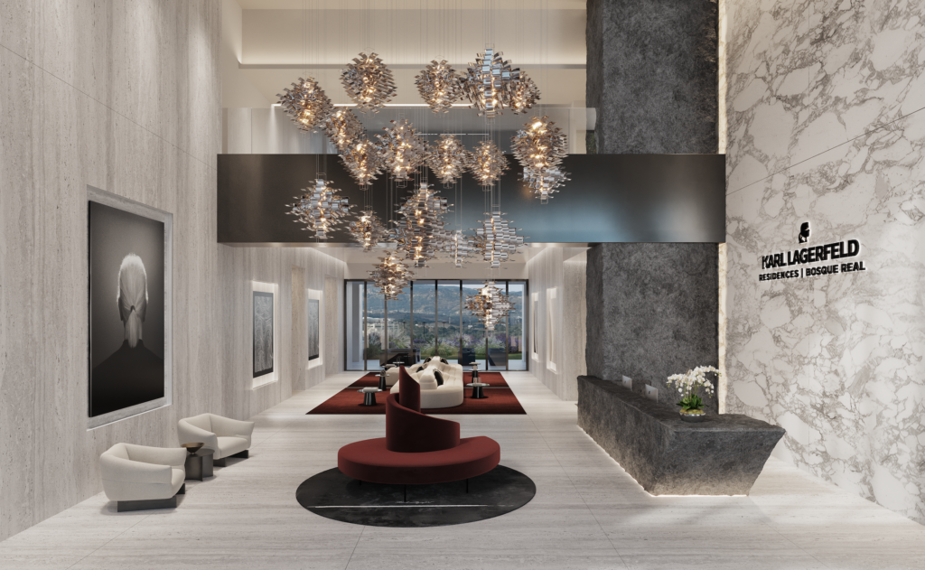 LOBBY_KARLS LAGERFELD - Petróleo y Energía Luxurious lobby with marble walls, dramatic metallic chandeliers, and red circular seating under a dark central beam, with a Karl Lagerfeld Residences sign in marble.