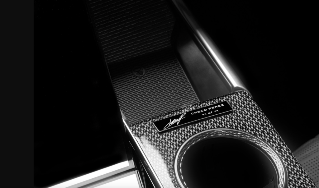 CADILLAC CHECO 3 - Petróleo y Energía Close-up of a carbon-fiber textured device with a round lens and a plaque reading'CHECO PEREZ 11 of 11' with a signature.