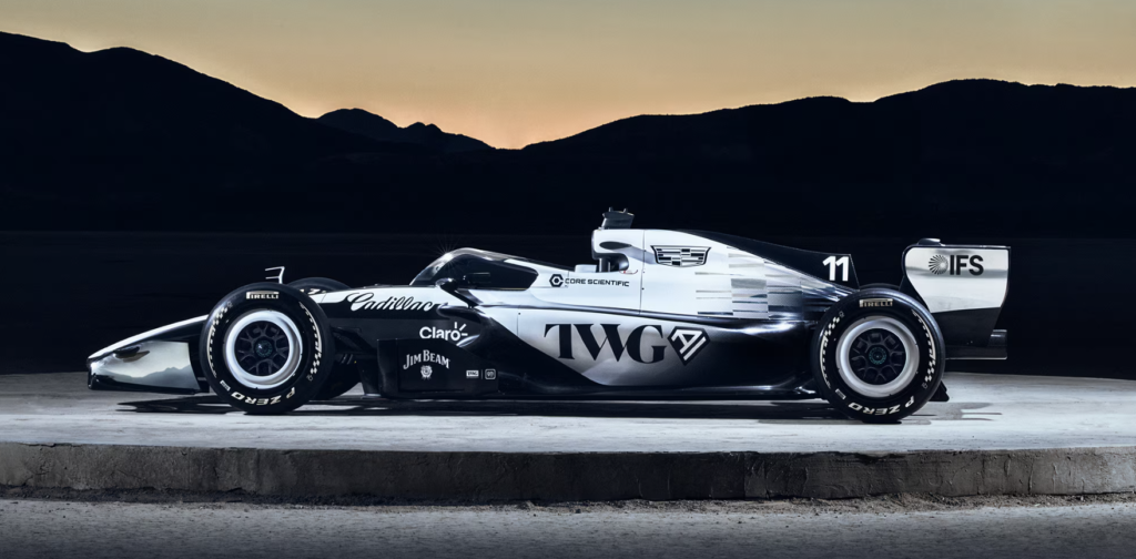 CHECO PÉREZ SHOW RUN 3 - Petróleo y Energía Side view of a white and black open-wheel race car on a concrete platform with a sunset and mountains in the background making a dramatic backdrop.