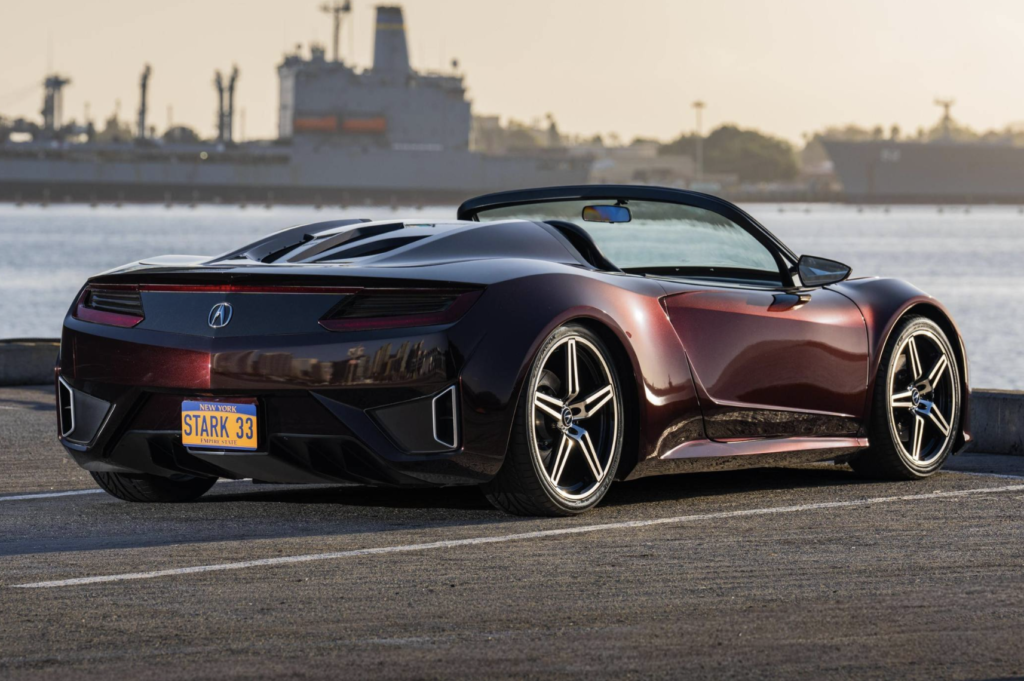 acura the avengers 2 - Petróleo y Energía Red convertible sports car parked by a harbor at sunset, license plate STARK 33, with ships in the distant background.