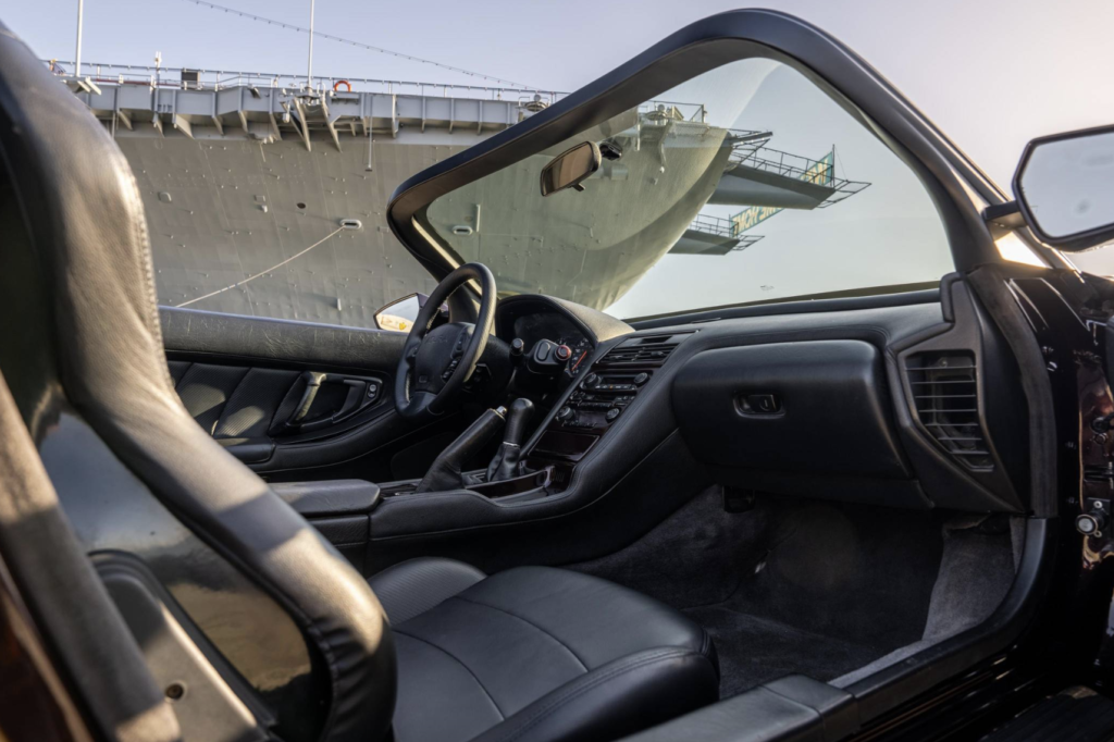 acura the avengers 2 - Petróleo y Energía Interior of a black leather car with the dashboard and steering wheel in the foreground; a large ship’s hull appears through the windshield/mirrored in the side window in the background.