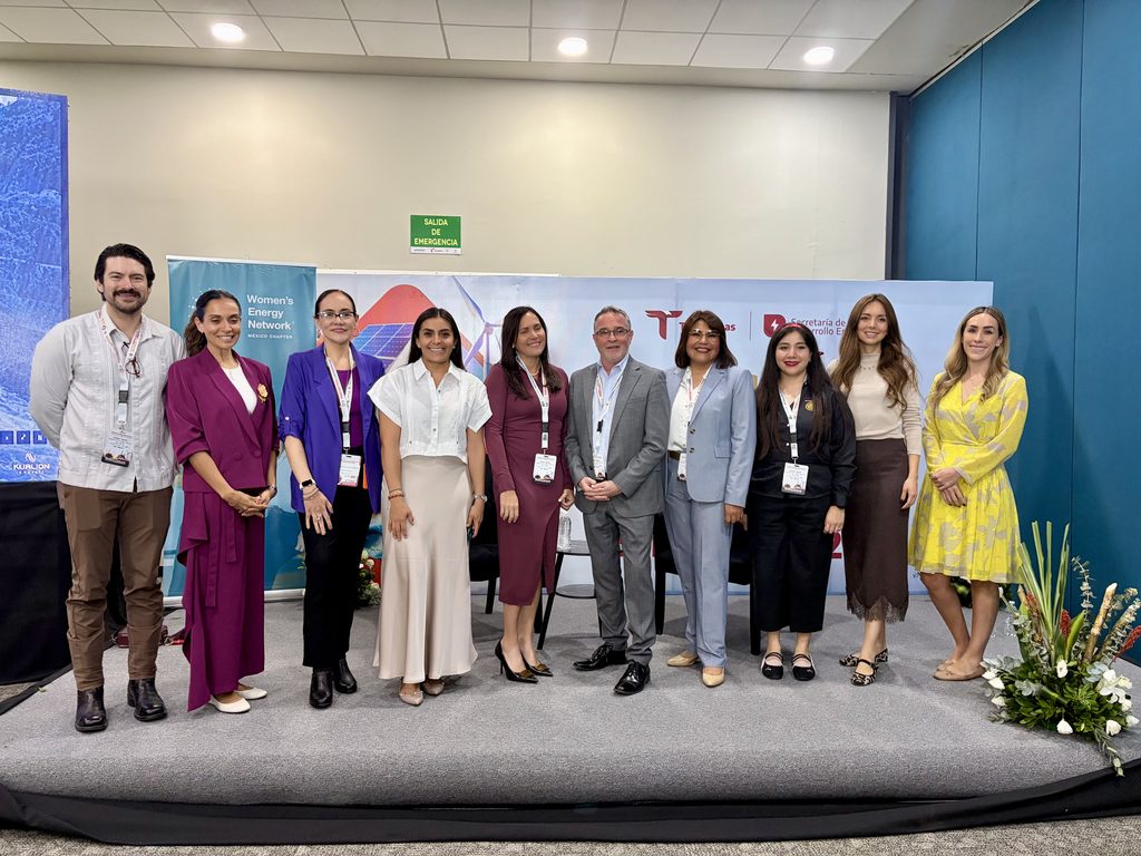 FullSizeRender 1 - Petróleo y Energía Group of ten professionals posing for a photo at a conference booth, all wearing lanyards and name badges.