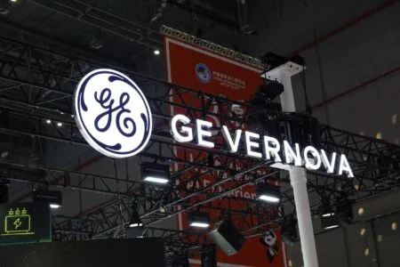 General Electric logo with 'GE Vernova' signage at an exhibition booth, mounted on a metal truss structure under venue lights.