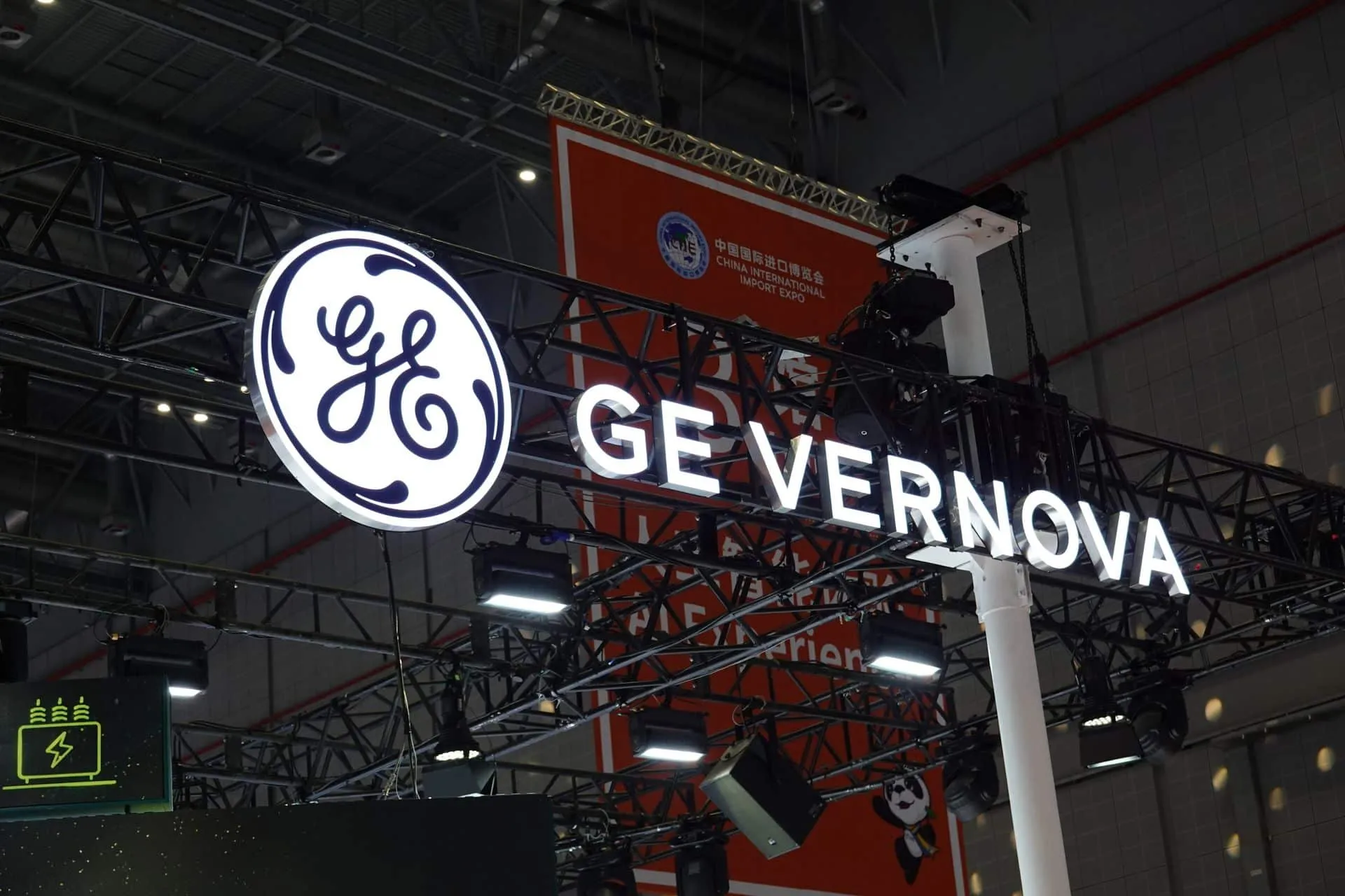 General Electric logo with 'GE Vernova' signage at an exhibition booth, mounted on a metal truss structure under venue lights.