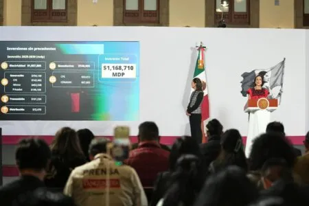 Speaker at a podium with the Mexican flag while a large investment infographic is shown on a screen behind her, addressed to an audience
