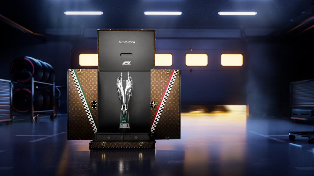LOUIS VUITTON x FORMULA 1_MEXICO_GP_1920x1080 - Petróleo y Energía Louis Vuitton display case with a silver Formula 1 trophy in front of monogram LV luggage, in a dim garage setting