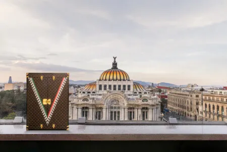 Louis Vuitton trunk with gold hardware and monogram pattern on a railing, skyline and a domed historic building in the background.