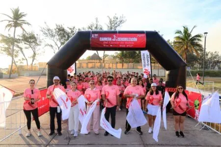 Group of people in pink shirts posing at the start line under a large inflatable arch for a breast cancer awareness 5K run.