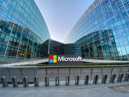 Microsoft logo displayed on a modern glass office complex with curved wings and a clear blue sky above