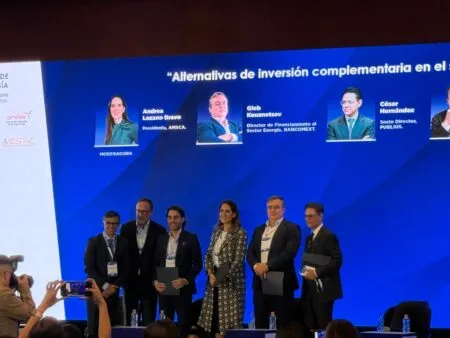 Six professionals pose on a conference stage with a blue backdrop featuring speaker portraits and names behind them.