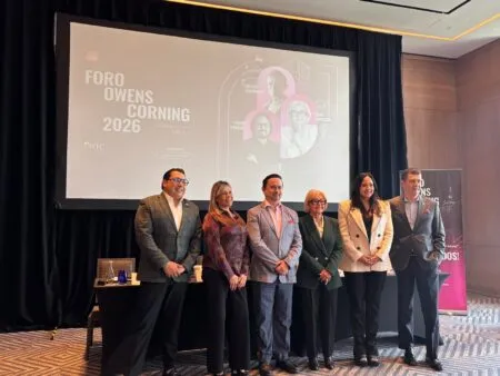 Six professionals in business attire pose on a conference stage in front of a large screen displaying Foro Owens Corning 2026 poster and graphics behind them.
