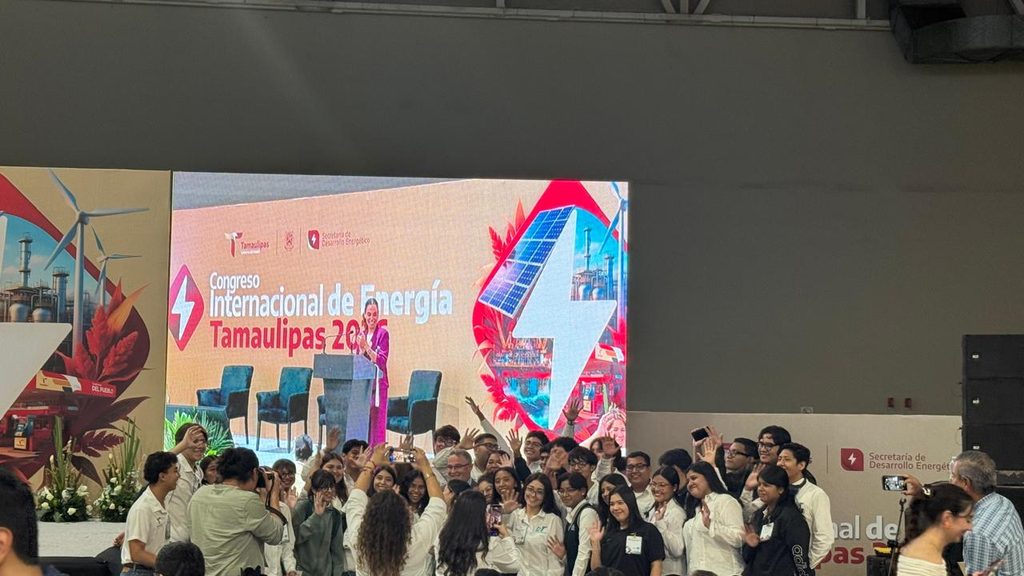 WhatsApp Image 2026-10-28 at 23830 PM - Petróleo y Energía Group of attendees in white shirts posing for a photo in front of a conference stage with a large LED screen displaying 'Congreso Internacional de Energía Tamaulipas'.