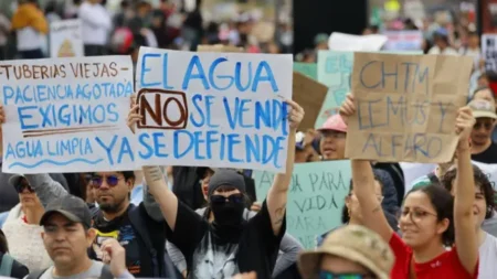 Protesters holding handmade signs in Spanish; central sign reads 'EL AGUA NO SE VENDE YA SE DEFIENDE' with other water-right messages visible in the crowd.