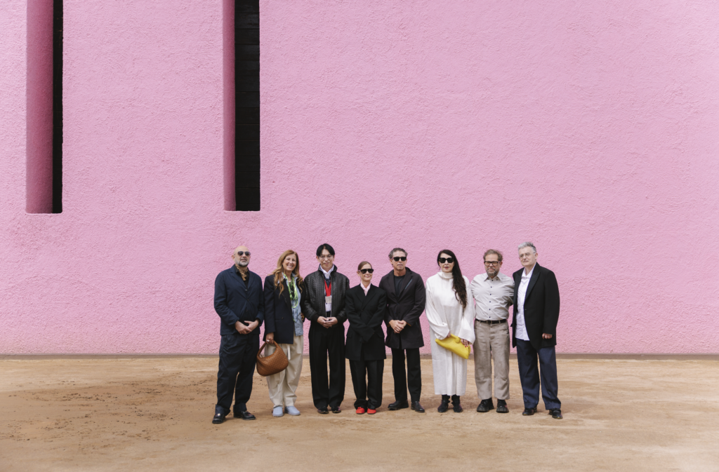 barragan prize 2026-10-12 a las 33020 pm - Petróleo y Energía Ten adults stand in a line in front of a textured pink wall outdoors, posing for a group photo.