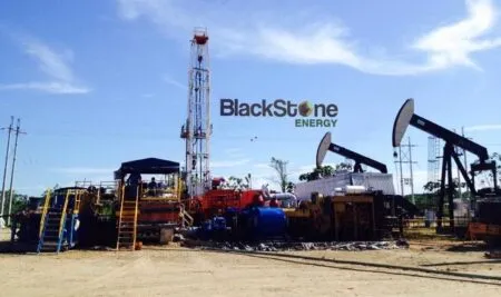 Oil drilling site with a tall derrick, pumpjacks, and industrial equipment under a blue sky; BlackStone Energy branding in the background.