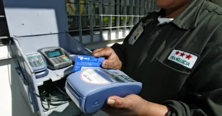 Worker in uniform uses a blue handheld card payment terminal, inserting a card into it.