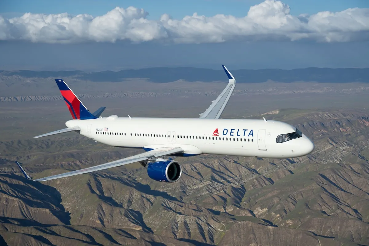 Delta airliner in flight over rugged desert mountains and a blue sky.