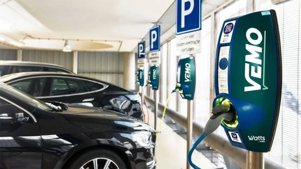 Electric vehicle charging station in a parking garage with blue VEMO/Vatts chargers connected to parked cars.