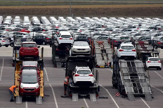Row of car carrier trailers loaded with white and colored cars in a large staging lot in the yard.