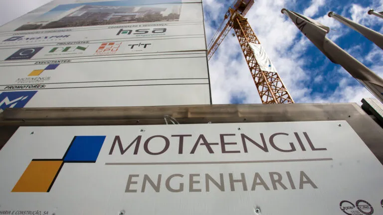 Construction company signboard with MOT A-ENGIL Engenharia e Construção in front of a crane and blue sky