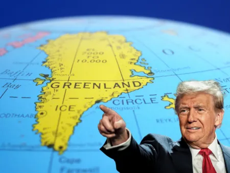 Man in a suit points to Greenland on a large globe.