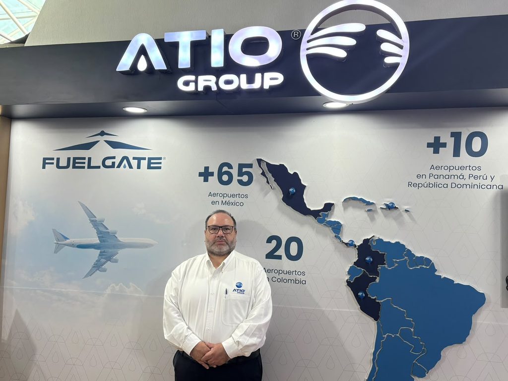skmjsg120946 PM - Petróleo y Energía Man in a white shirt stands in front of an ATIO Group display featuring a map of Latin America and airport counts in Mexico and Colombia? (informational/brand backdrop)